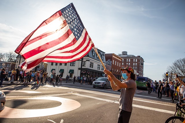 A man waving a flag to passing vehicles in downtown Burlington - LUKE AWTRY