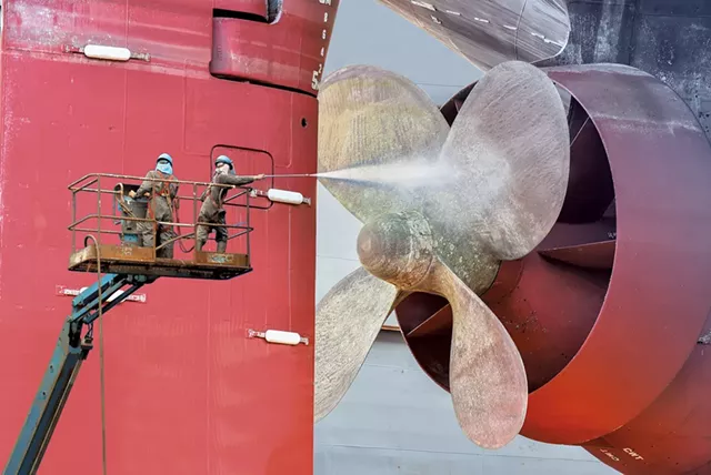 Shipyard workers cleaning a ship by jet water - COURTESY