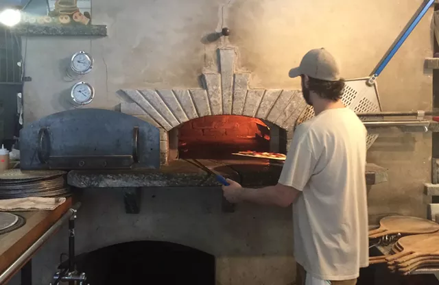 A Folino's staffer puts a pizza in the wood-fired oven - SUZANNE PODHAIZER