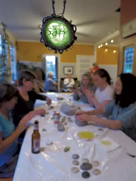 Friends making SamStones from clay beneath a glass emblem bearing Sam's name - MATTHEW THORSEN
