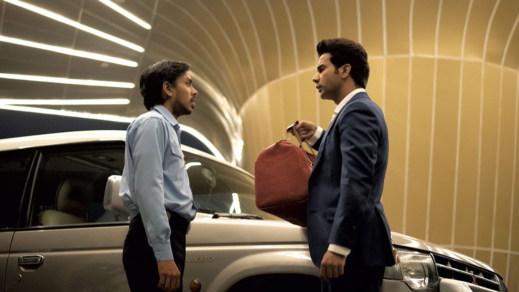 Balram and Ashok stand face-to-face while exchanging a bag of money. 