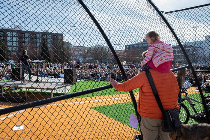 A father, daughter, and dog watch the strike from behind the Cal Anderson Park backstop.