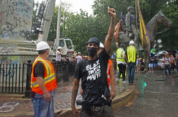 A young man raises his fist in the pouring rain just after the removal of the Stonewall Jackson statue July 1. - SCOTT ELMQUIST
