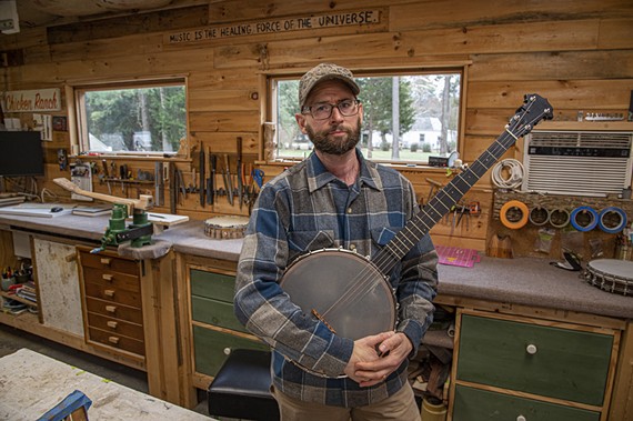 Banjo maker J. Tyler Burke holds one of his creations inside his Varina garage. A handmade sign on the wall reads: "Music Is The Healing Force Of The Universe."