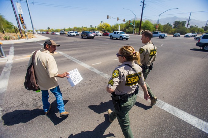 A panhandler, left, is escorted across the street by Pima County Sheriff’s Deputy Daniel Sharp Jr., and Sgt. Erin Gibson, after talking about the potential new signs that may prohibit individuals from standing in medians in unincorporated areas of Pima County.