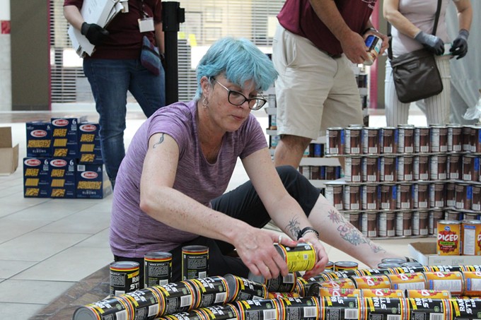 A volunteer helps build a “canstructure” at the Community Food Bank of Southern Arizona’s “Build Day,” at the Park Place Mall on Saturday, June 4. The summer fundraiser, Canstruction, is a friendly building competition among local architects, engineers and builders to raise awareness for food insecurity during the summer months. - PHOTO BY KATYA MENDOZA